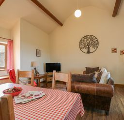 A living room with a table, sofa, and television at Poppy Cottage in Caeathro near Caernarfon