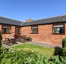 A brick house with a small garden and picnic bench at 2 Pines Farm Cottages in Ulleskelf