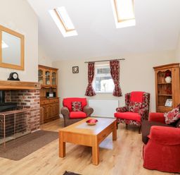 A living room with red and brown seating around a wooden coffee table and a brick fireplace at 2 Pines Farm Cottages in Ulleskelf
