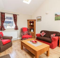 A living room with a wooden coffee table sofa armchairs and cupboard with curtains on window at 2 Pines Farm Cottages Ulleskelf