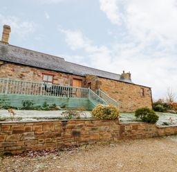 A stone house with a green wooden deck and stairs surrounded by a garden and gravel path at The Dairy in Milton near Brampton