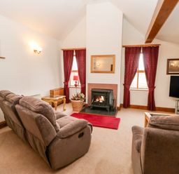 A living room with two brown sofas a fireplace a television and red curtains at The Dairy in Milton near Brampton