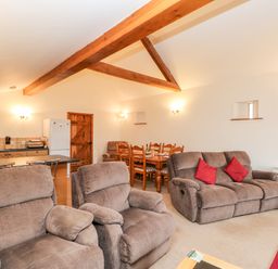 A living room with brown sofas and red cushions a dining table and chairs and a kitchen area at The Dairy in Milton near Brampton