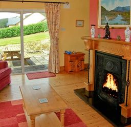 A living room with a fireplace a wooden coffee table a red sofa and a sliding glass door at Heron's Nest in Inch County Kerry