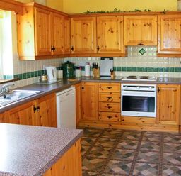 A kitchen with wooden cabinets a white oven a stainless steel sink and tiled floor at Herons Nest in Inch County Kerry