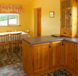 A kitchen with wooden cabinets a dining table with chairs and a window at Heron's Nest in Inch County Kerry