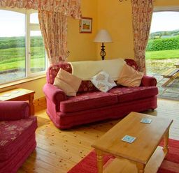 A living room with red sofas wooden coffee table floor lamp and large windows at Herons Nest in Inch County Kerry