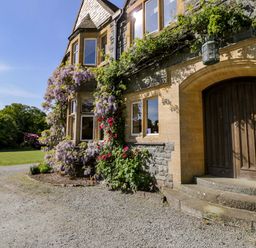 The exterior of a stone house with a wooden door climbing plants and a gravel driveway at Plas Gwynfryn in Llanbedr