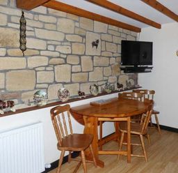 A dining area with wooden table and chairs stone wall and wall mounted television at The Stable in Aislaby near Whitby