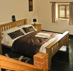 A bedroom with a wooden bed and bedside tables with lamps at The Byre in Llanddewi Skirrid near Abergavenny