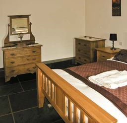 A bedroom with wooden bed and dressers a lamp and folded towels at The Byre in Llanddewi Skirrid near Abergavenny