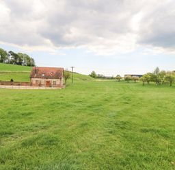 A small brick house with a red roof surrounded by a fenced green field and trees at Shepherd's Barn Between Milborne St Andrew and Winterborne Whitechurch