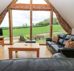 A living room with black leather sofas a wooden coffee table a television and large windows overlooking green fields at Shepherd's Barn Between Milborne St Andrew and Winterborne Whitechurch