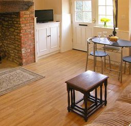 A room with a stone and brick fireplace a small black table a dining table with two chairs and a sofa at Candy Cottage Thornford near Sherborne