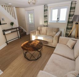 A living room with two beige sofas a round wooden coffee table a TV mounted on the wall stairs a floor lamp and a window with plaid curtains at Saddlers Cottage Berllandeg Farm Clunderwen near Narberth