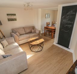 A living room with two beige sofas a wooden coffee table a tripod lamp and a dining table at Saddlers Cottage Berllandeg Farm