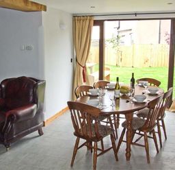A dining area with a wooden table set for six and leather armchairs near sliding glass doors at Bushmills in Kerry's Gate near Abbey Dore