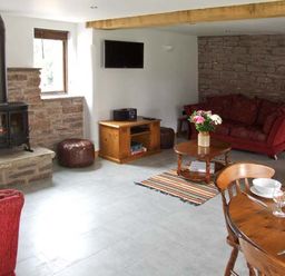 A living room with a wood-burning stove red sofas wooden coffee table with flowers and a dining table at Bushmills in Kerrys Gate near Abbey Dore