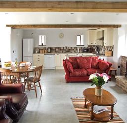 An open plan kitchen and living area with wooden dining table and chairs red sofa and wood stove at Bushmills in Kerrys Gate near Abbey Dore