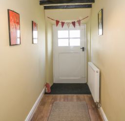 A narrow hallway with yellow walls wooden floor a white door with window panels and heart decorations at Ty Fferm Bodlasan Llanfachraeth near Valley