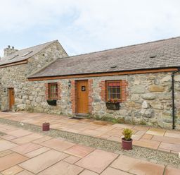 A stone cottage with wooden doors and windows surrounded by a stone patio with potted plants and a lamp post at Daffodil Cottage in Caeathro near Caernarfon