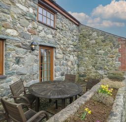 An outdoor seating area with a wooden table and chairs at Daffodil Cottage Caeathro near Caernarfon