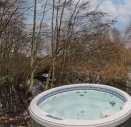 An outdoor hot tub near a body of water surrounded by leafless trees at The Lakeside Yurt in Beckford