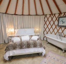 A bedroom with a bed a fur throw white curtains and a bathtub at The Lakeside Yurt in Beckford