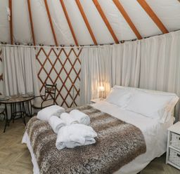 A bedroom inside a yurt with a bed with white linens and fur throw and small dining table with two chairs at The Lakeside Yurt in Beckford