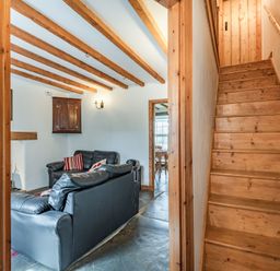 A living room with black leather sofas and wooden ceiling beams next to wooden stairs at Ty Capel Jeriwsalem in Bronaber near Trawsfynydd