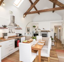 Kitchen and dining area with wooden table white chairs and exposed wooden beams at Beudy Hywel in Llanrug near Llanberis