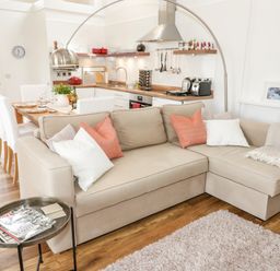 A beige sectional sofa with pillows in an open-plan living room and kitchen at Beudy Hywel in Llanrug near Llanberis