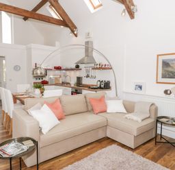 An open plan living room and kitchen with a beige sofa dining table and kitchen appliances at Beudy Hywel in Llanrug near Llanberis