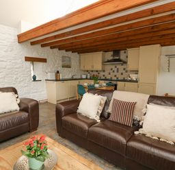 A living room with brown leather sofas and a kitchen with wooden cabinets at Bwthyn Bach in Newport