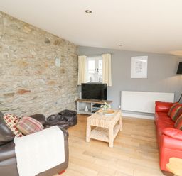A living room with a red sofa a brown armchair a woven coffee table and a television on a stand at Y Cwtch in Newport