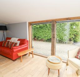 A living room with a red sofa and a beige armchair near large windows showing a hedge outside at Y Cwtch in Newport