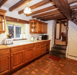 A kitchen with wooden cabinets tiled floor and a cream countertop at Nant Cottage in Llanrwst near Betws-y-Coed
