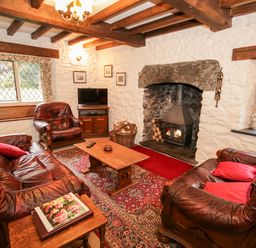 A living room with leather sofas a wooden coffee table a fireplace with a wood stove and a television at Nant Cottage in Llanrwst near Betws-y-Coed