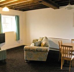 A living room with a striped armchair a sofa a round wooden dining table with chairs and a wall-mounted TV at Hendre Aled Cottage 3 Llansannan