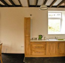 A kitchen with wooden cabinets a dining table with chairs and kitchen appliances at Hendre Aled Cottage 3 in Llansannan