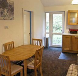 A dining area with a wooden table and four chairs next to a kitchen with wooden cabinets and glass door at Hendre Aled Cottage 1 in Llansannan near Llanrwst