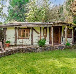 A small rustic house with wooden beams windows and a door surrounded by greenery and a grassy lawn at Brookbank Folly in Mitcheldean