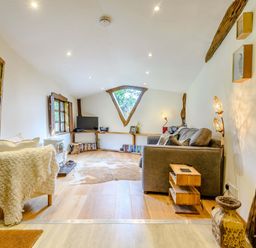 A living room with a gray sofa a white armchair a wooden coffee table a TV on a wooden shelf and a triangular window at Brookbank Folly in Mitcheldean