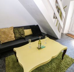 A living room with black sofa cushions and a yellow coffee table on a green rug next to a staircase and front door at Hollie Cottage in Haltwhistle