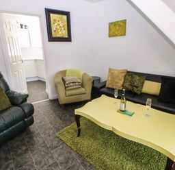 A living room with green armchair black sofa yellow coffee table and entrance to a kitchen at Hollie Cottage in Haltwhistle