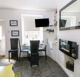 A dining area with a round table and four black chairs a wall-mounted TV and a fireplace at Hollie Cottage in Haltwhistle