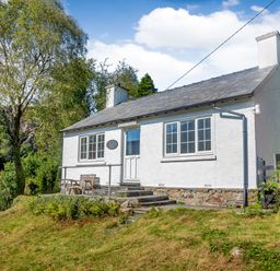 A white cottage with two chimneys and steps leading to the door surrounded by trees at Penlan in Beddgelert