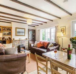 A living room with two brown leather sofas a wooden dining table with flowers and wine at Penlan in Beddgelert