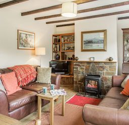 A living room with two brown leather sofas a wooden coffee table and a stone fireplace at Penlan in Beddgelert
