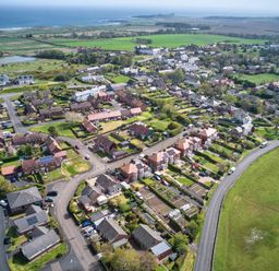 An aerial view of a residential neighborhood with houses gardens roads and fields near the coast at Cra-na-ge in Embleton
